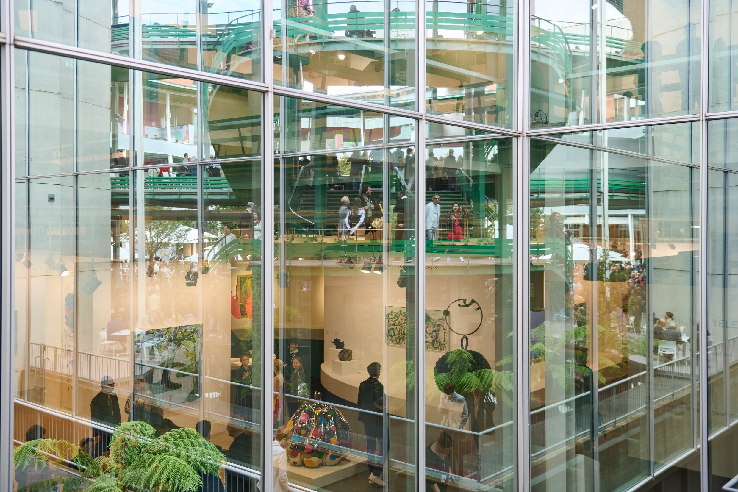 A color photo shows art, art fair booths, and plants amid glass.