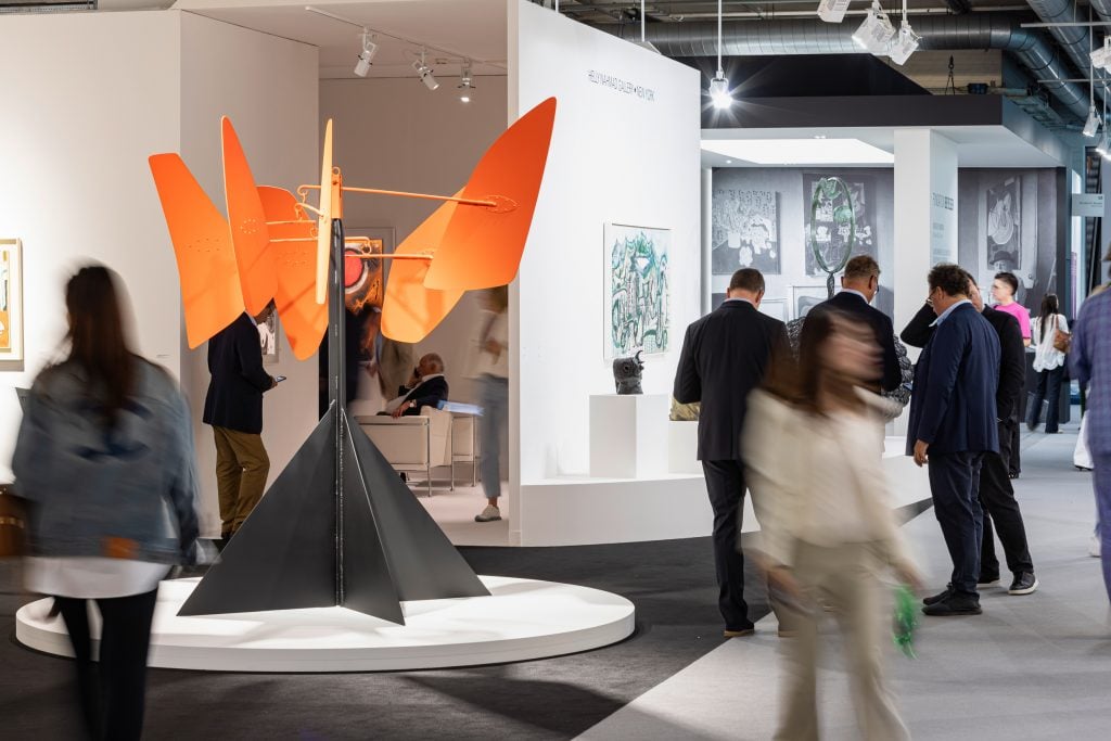 people walk around a large sculpture with orange flags at an art faire