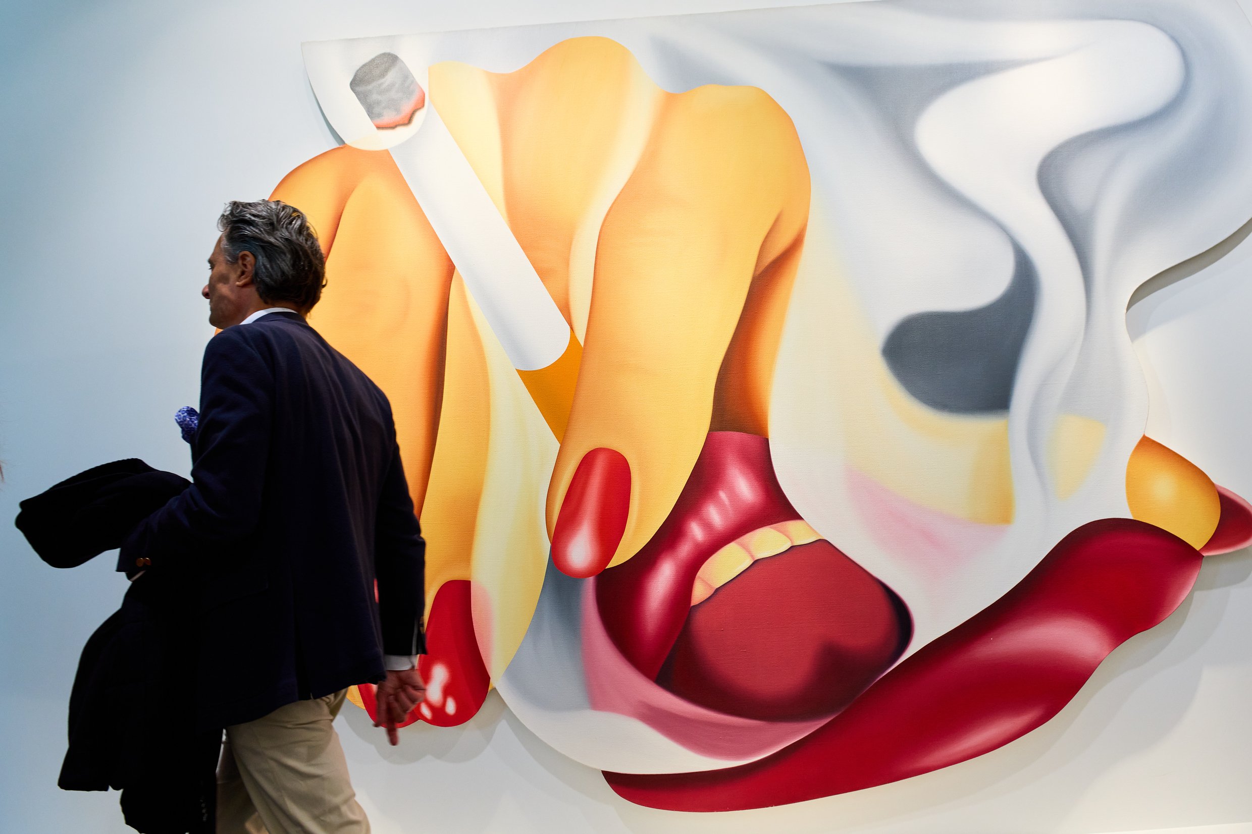 a man walks in front of a painting of a woman blowing smoke from a cigarette