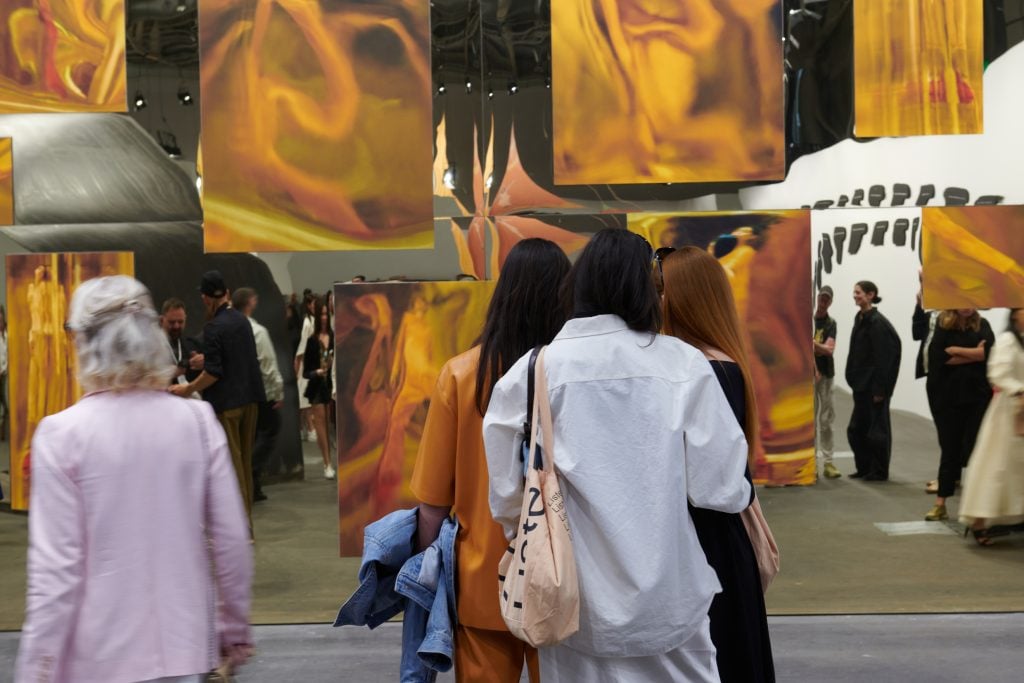 people walk under an installation of hanging orange paintings