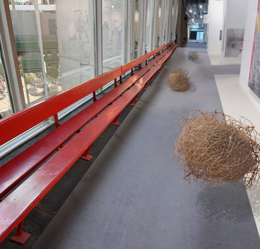 In a color photo, digital tumbleweeds roll down an empty aisle of a white-walled art fair.