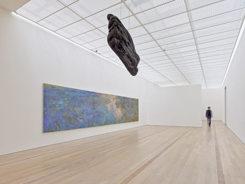a bronze sculpture in the shape of driftwood is suspended in the air alongside an impressionist painting of waterlilies