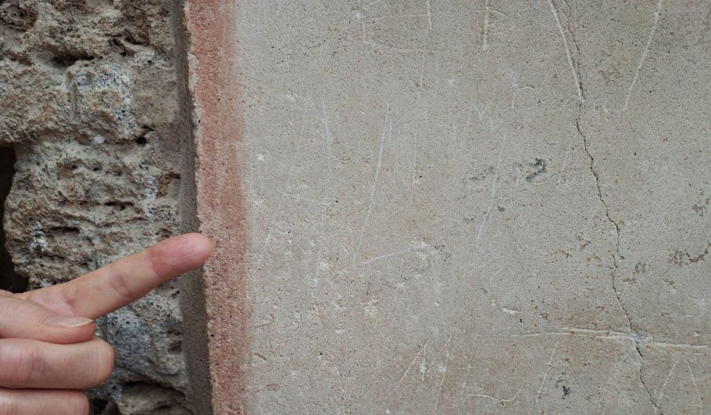 a finer points to a plain plaster wall in which you can faintly see the letters ALI inscribed, there are also other faint carvings from over the years