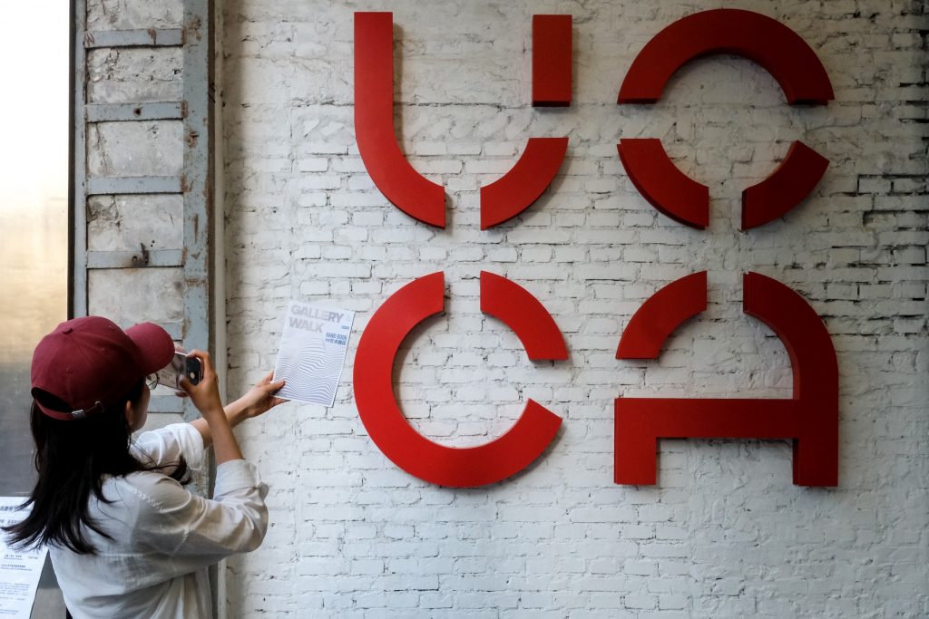 A woman points a camera at a wall with the letter UCCA on it