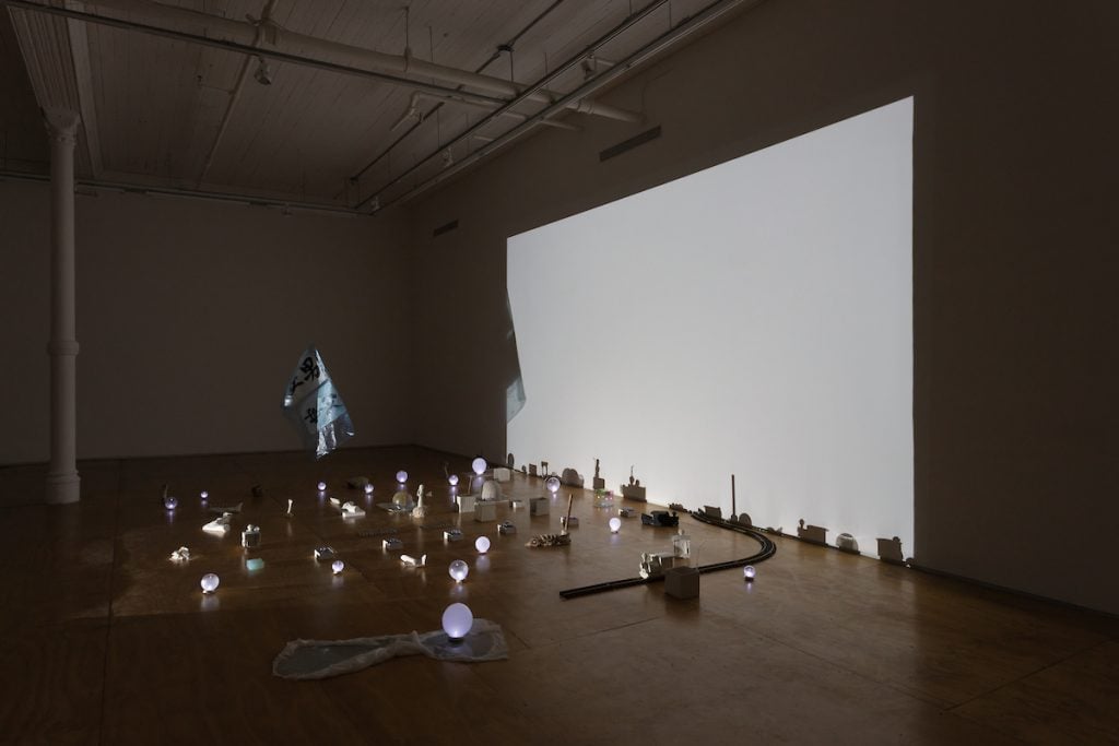 A glowing white screen is at the back of a dark room. Small objects are on the floor.