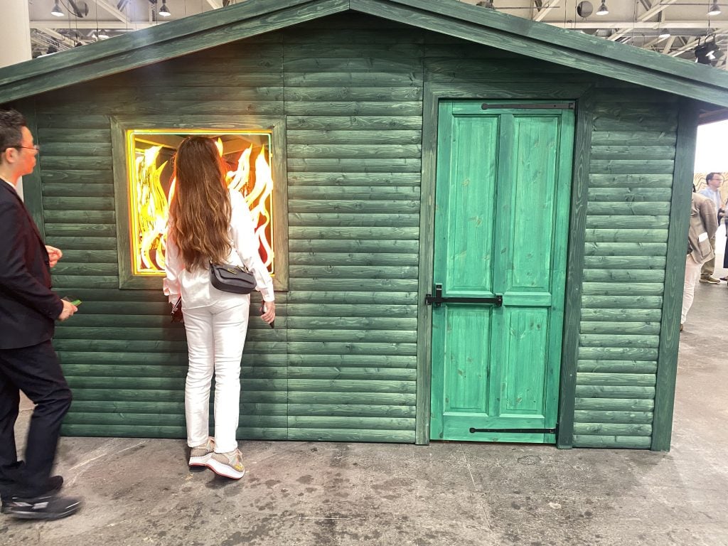 A woman peers in the window of a green wooden cabin with neon flames on the windows