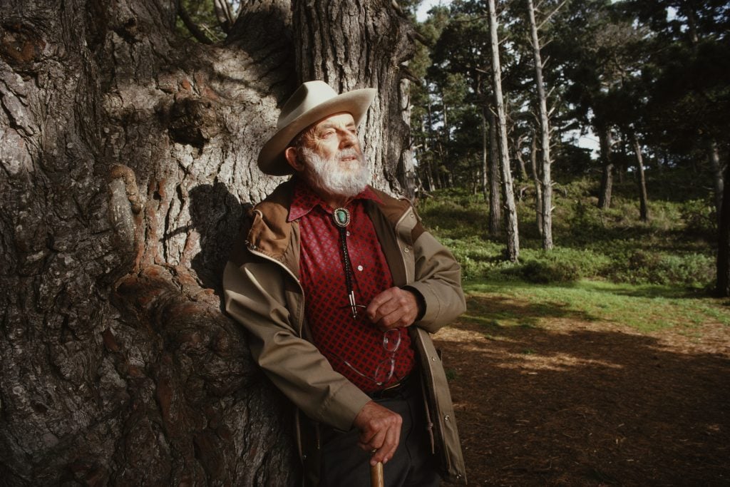 A bearded man, photographer Ansel Adams, leaning against a tree