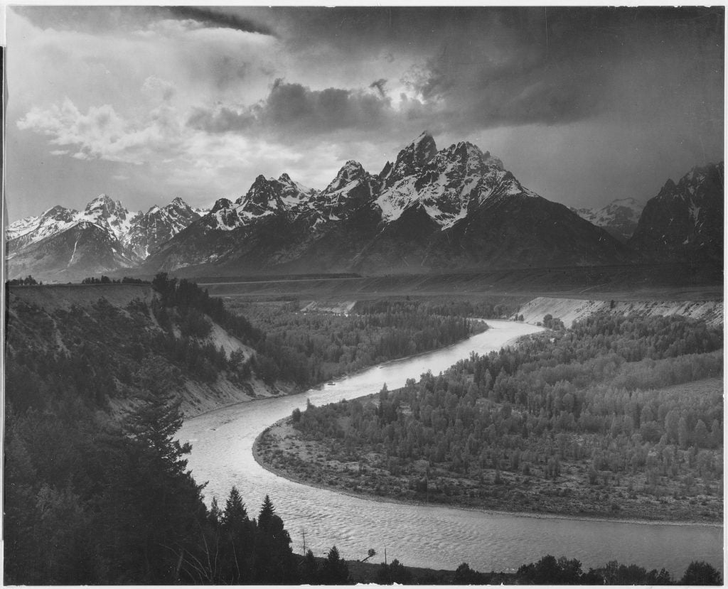 A black and white photograph of the Tetons mountain range in the background and Snake River in the foreground