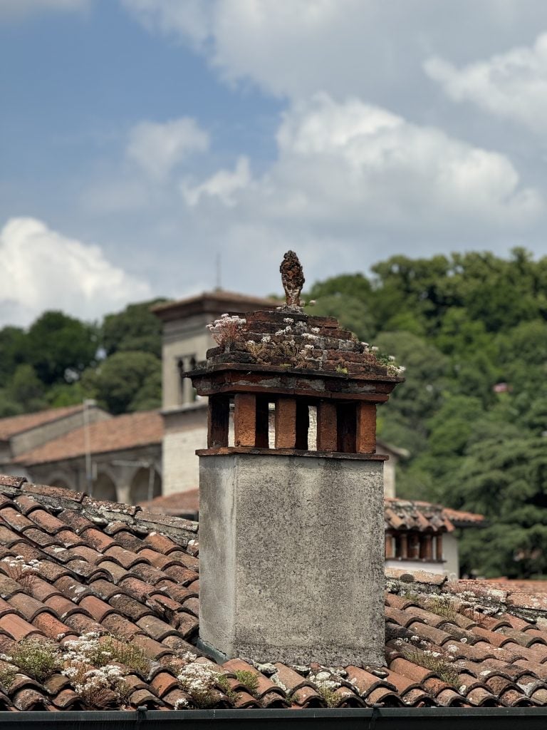 View out of the studio of Cindy Phenix showing a pinecone figurine installed at the top of a chimney.