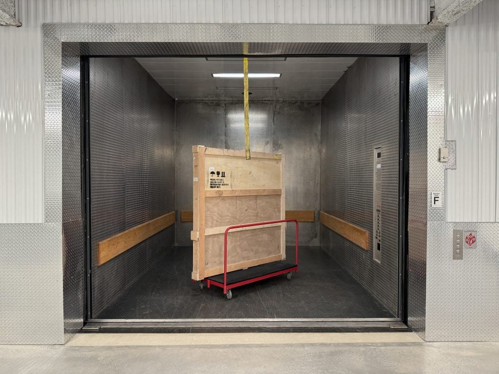 Inside one of the freight elevators at Fine Art Shippers with a dolly carrying a crate inside.