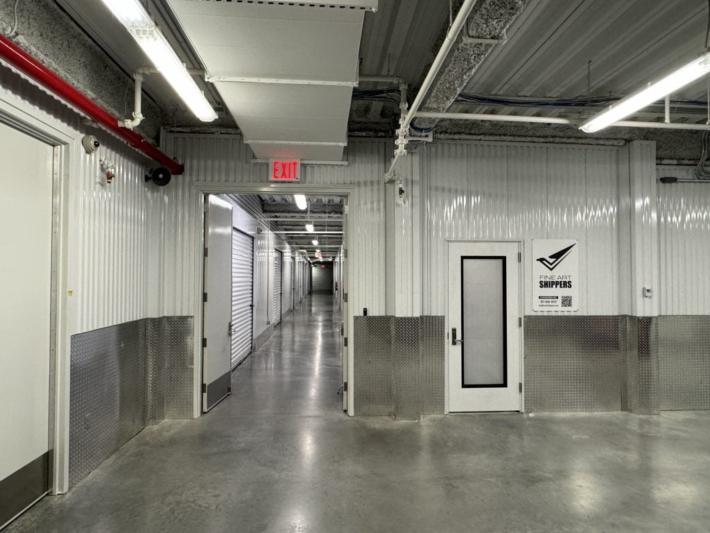 Inside a storage area and hallway with metal rolling doors down a long hallway with concrete floors.