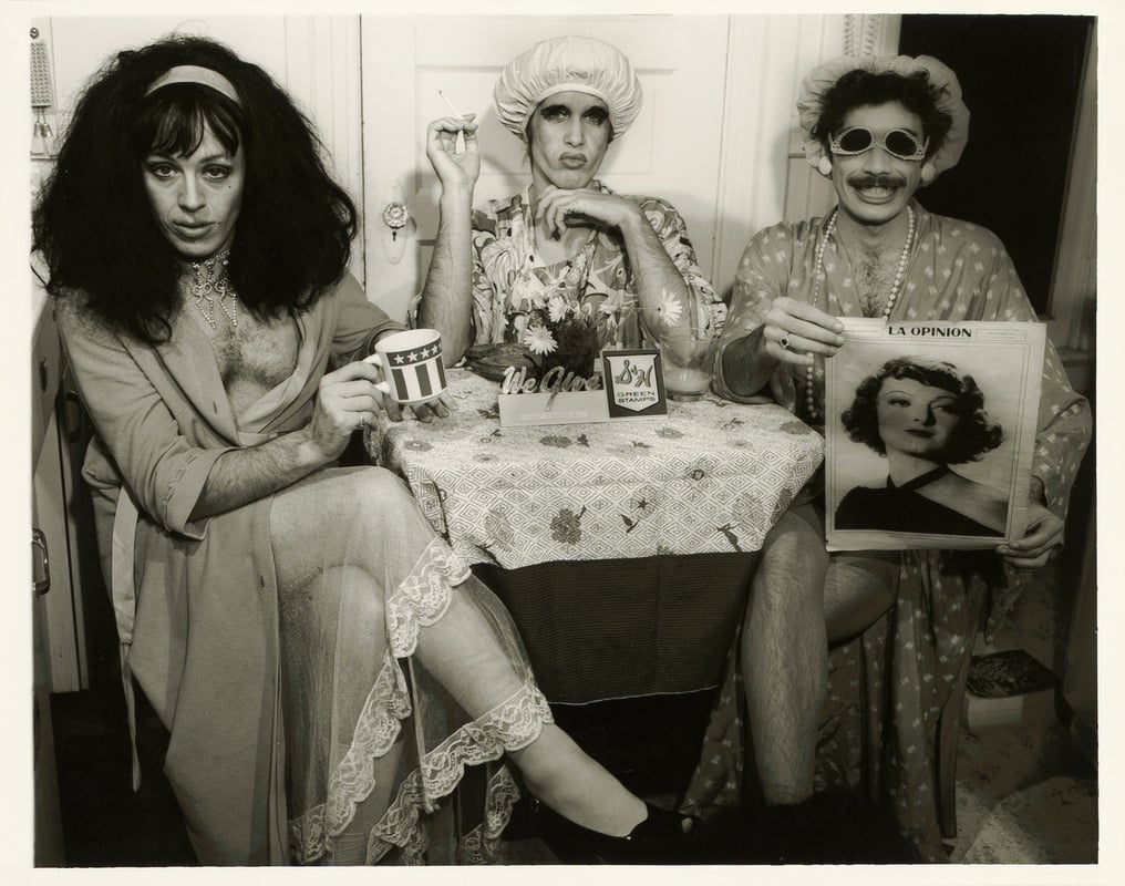 the drag queens sitting at a table with tea