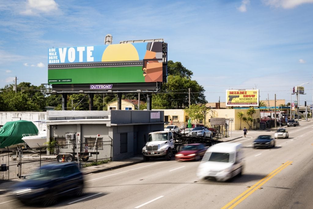 A photo of a billboard with a Black man's face and text urging the viewer to vote