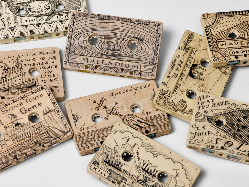 Scrimshaw cassette tapes by Duke Riley scattered on a white surface