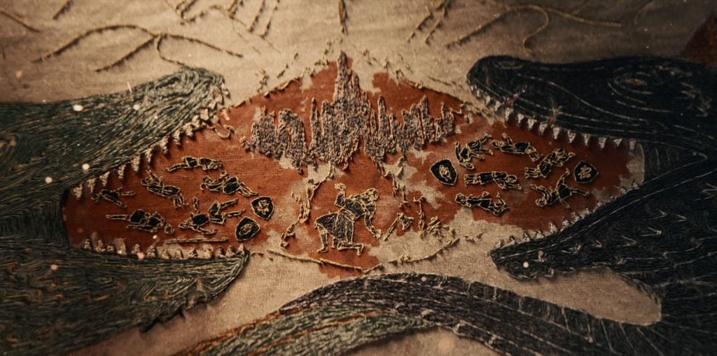An embroidered tapestry showing people dying in front of a citadel, the entire scene framed by two dragons