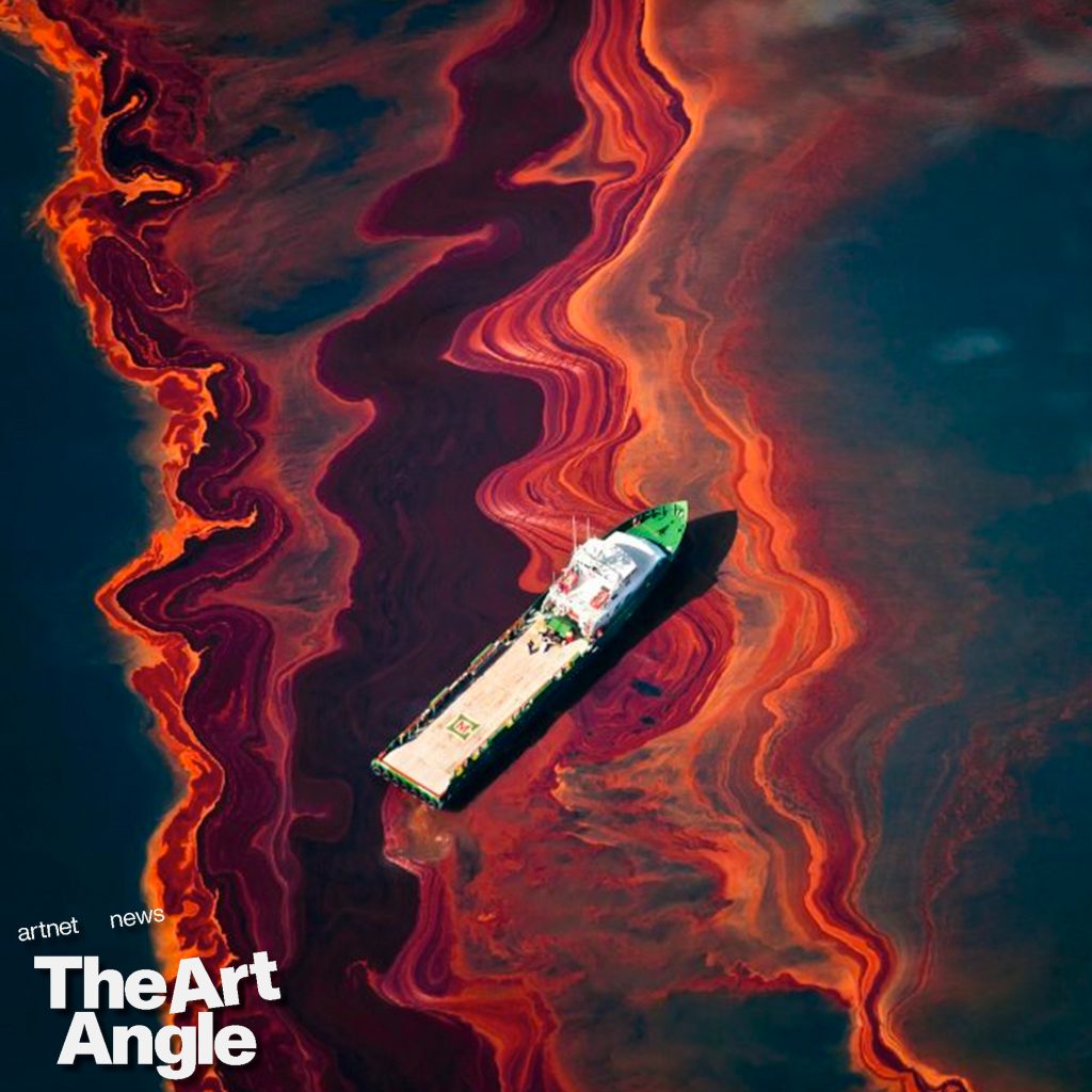 an aerial view of a red-colored oil spill in a turquoise body of water with a lone cargo ship