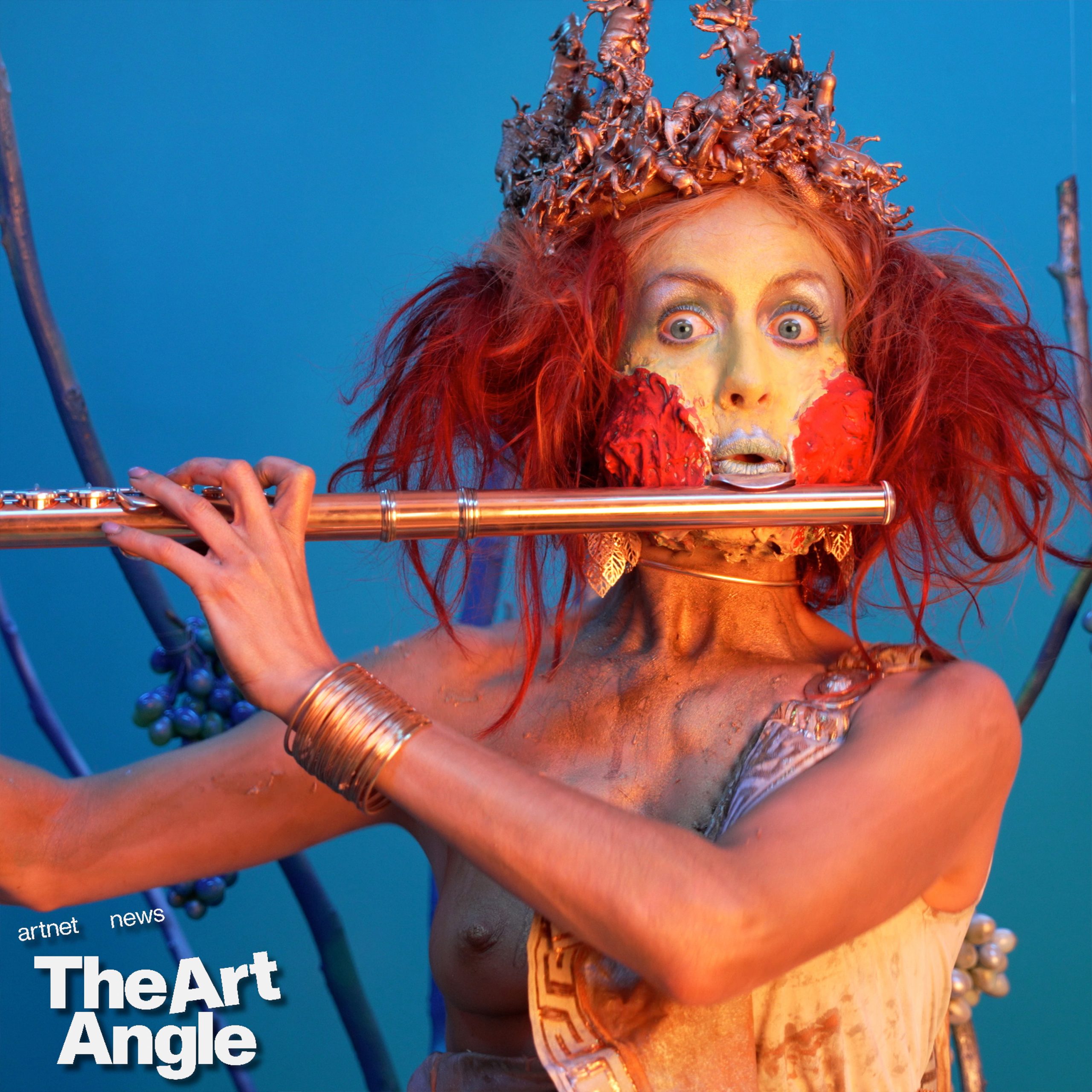 a woman dressed as a pied piper with a red wig and beard plays the flute against a blue background