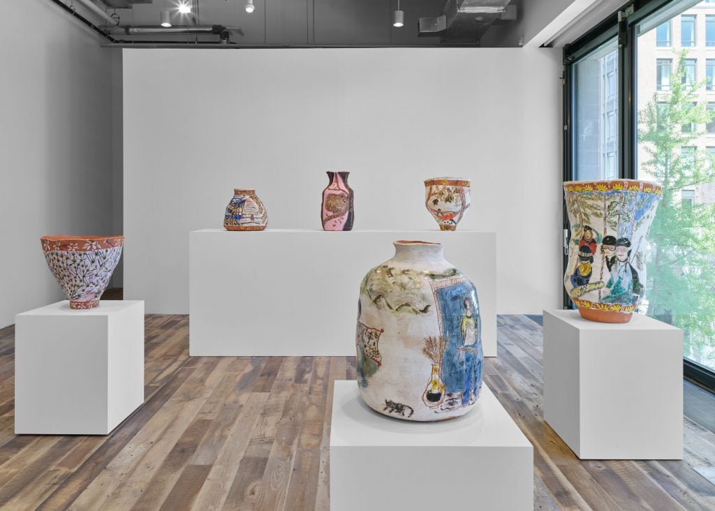 Installation view of solo exhibition of terracotta pots by artist Jennifer Rochlin; six are viewable with three on a plinth in a row along the back and three on separate pedestals in the foreground and a window wall along the right.