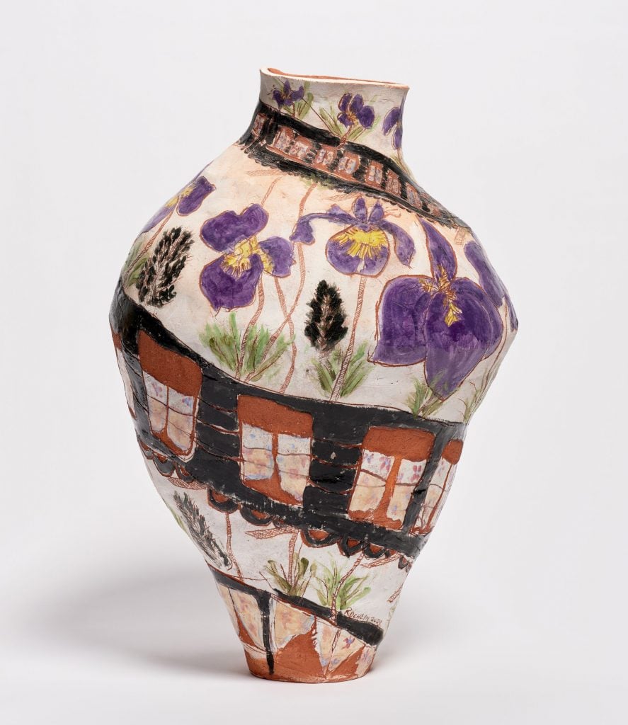 A terracotta pot by Jennifer Rochlin with rows of roughly painted train cars circling the vessel surrounded by large purple irises.