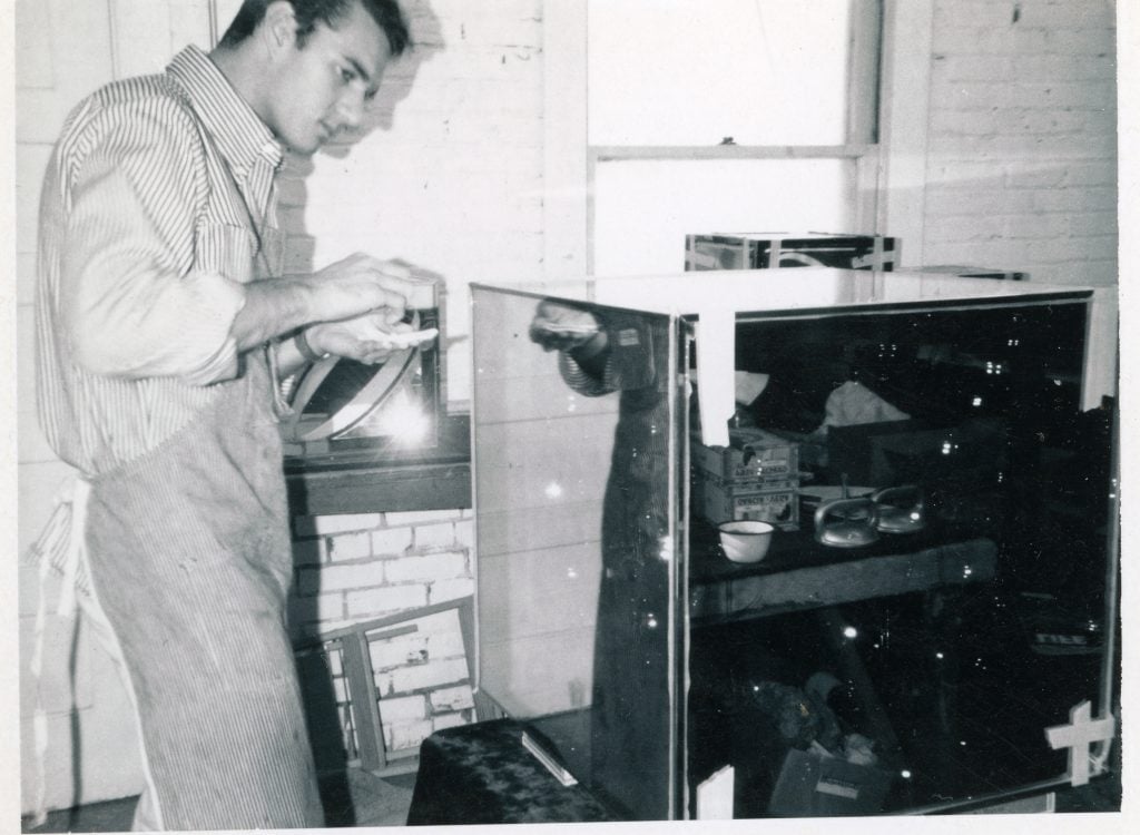 black and white photograph of artist larry bell gluing a glass cube