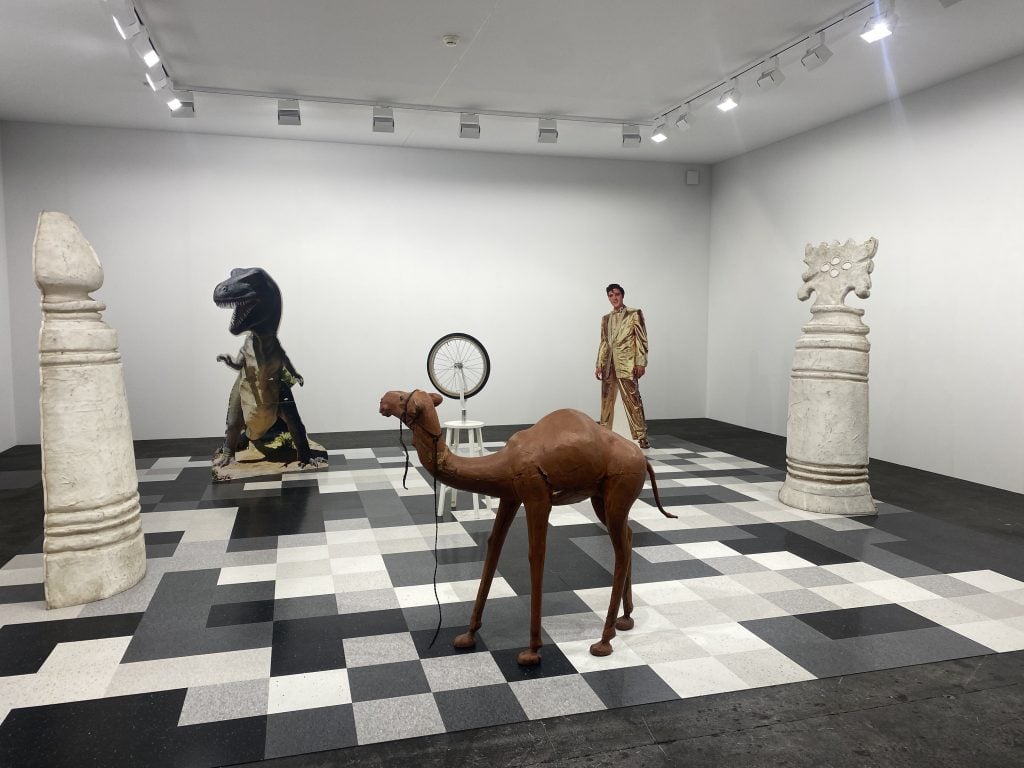 A larger than life chess set with a camel, a t.rex, elvis presley, and more as the pieces