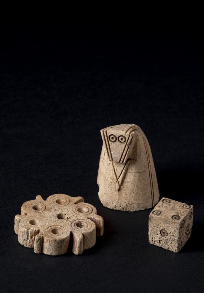 Three medieval game-playing pieces including a die, a chessman, and a flower-shaped item