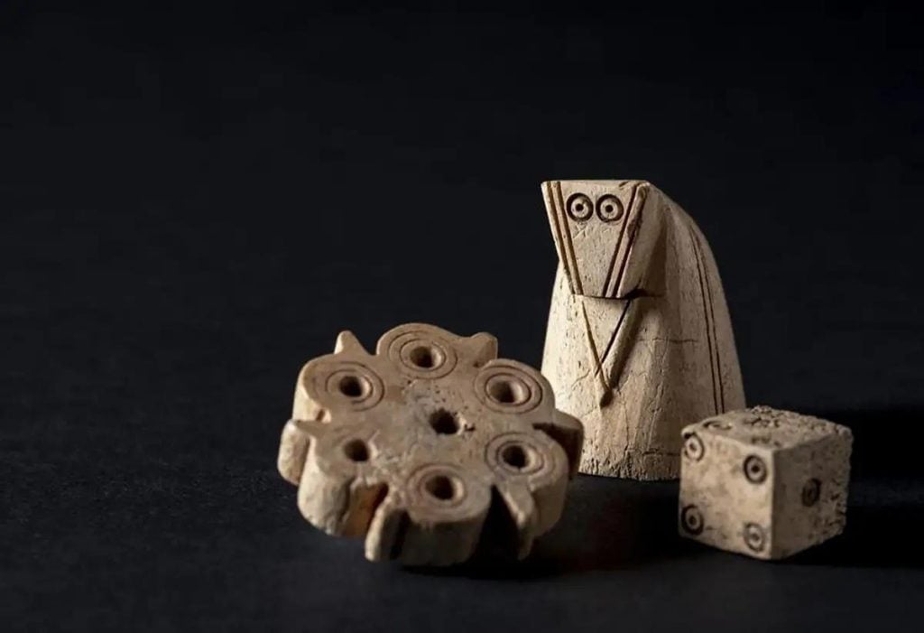 Three medieval game-playing pieces including a die, a chessman, and a flower-shaped item