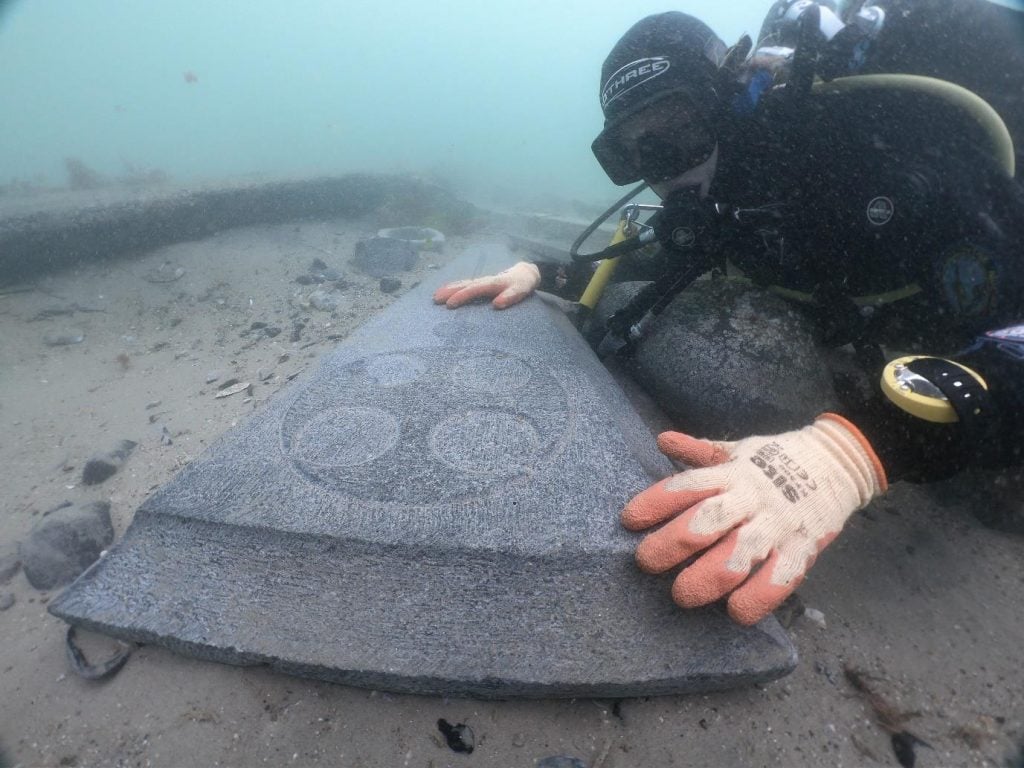 A diver underwater reaching out for a large stone slab