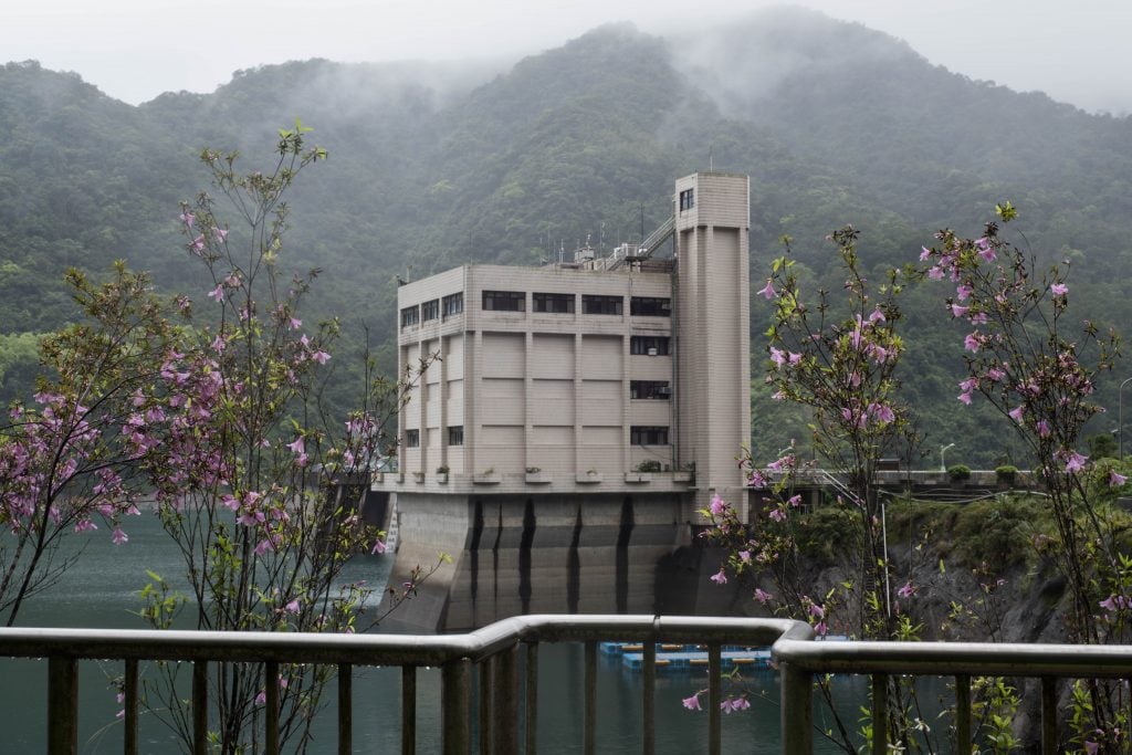 photograph of azalea trees in the foreground and the feitsui dam in the background