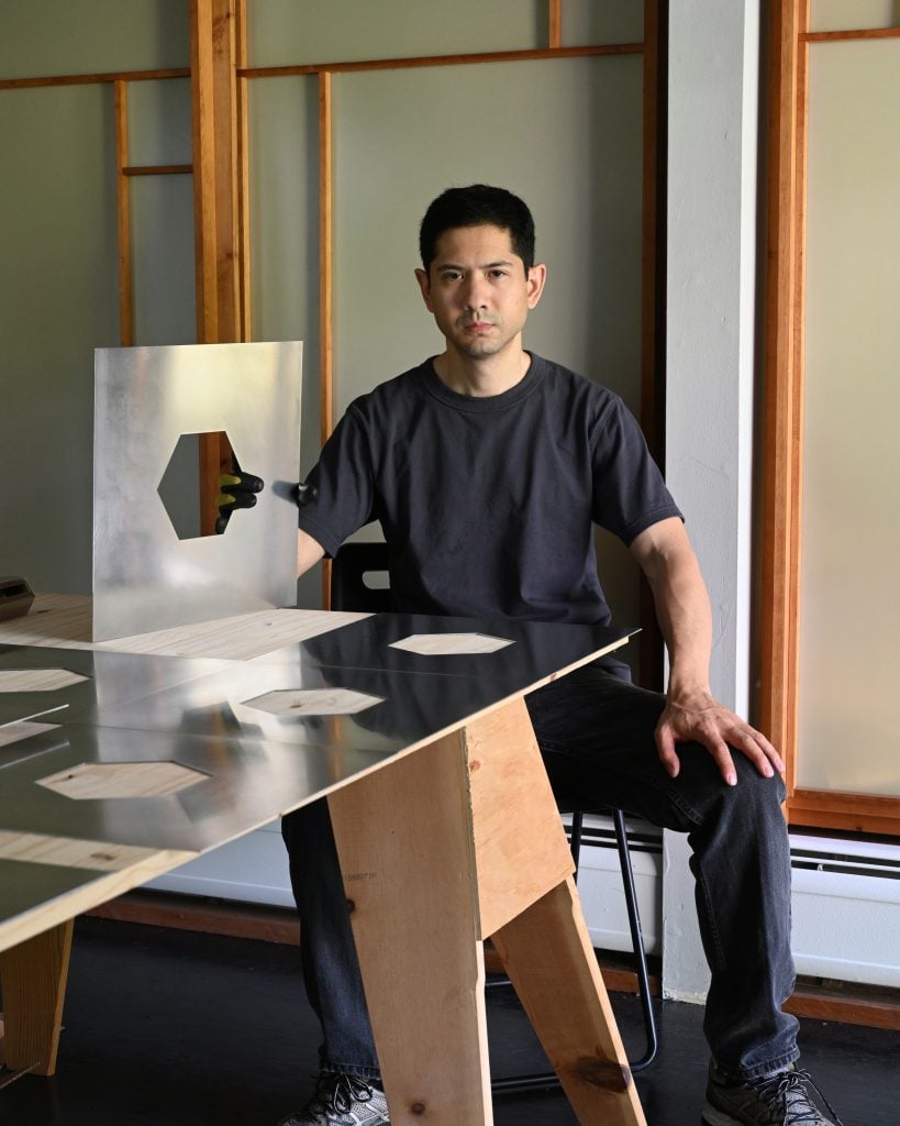 portrait of artist michael wang sitting by a table holding a steel plate