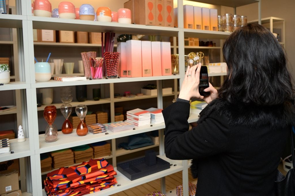 A woman points a cell photo at a shelf full of colorful products