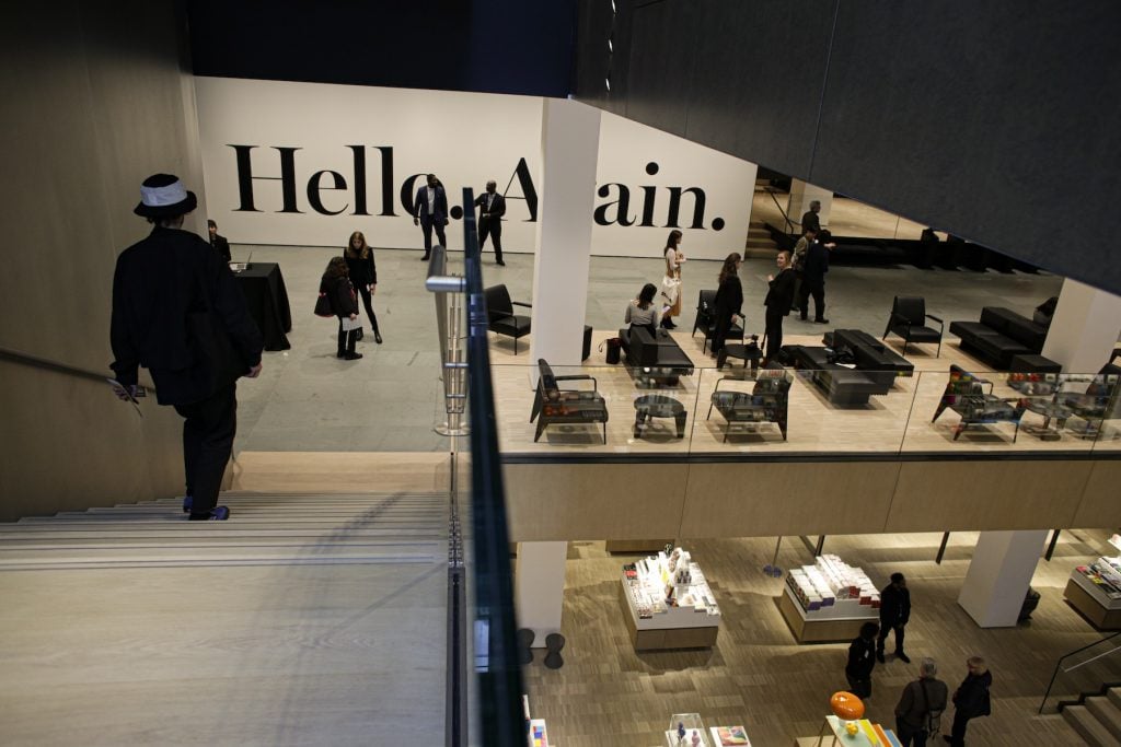 A large museum gallery with the words "HELLO AGAIN" on the wall, viewed from the top of a concrete stair