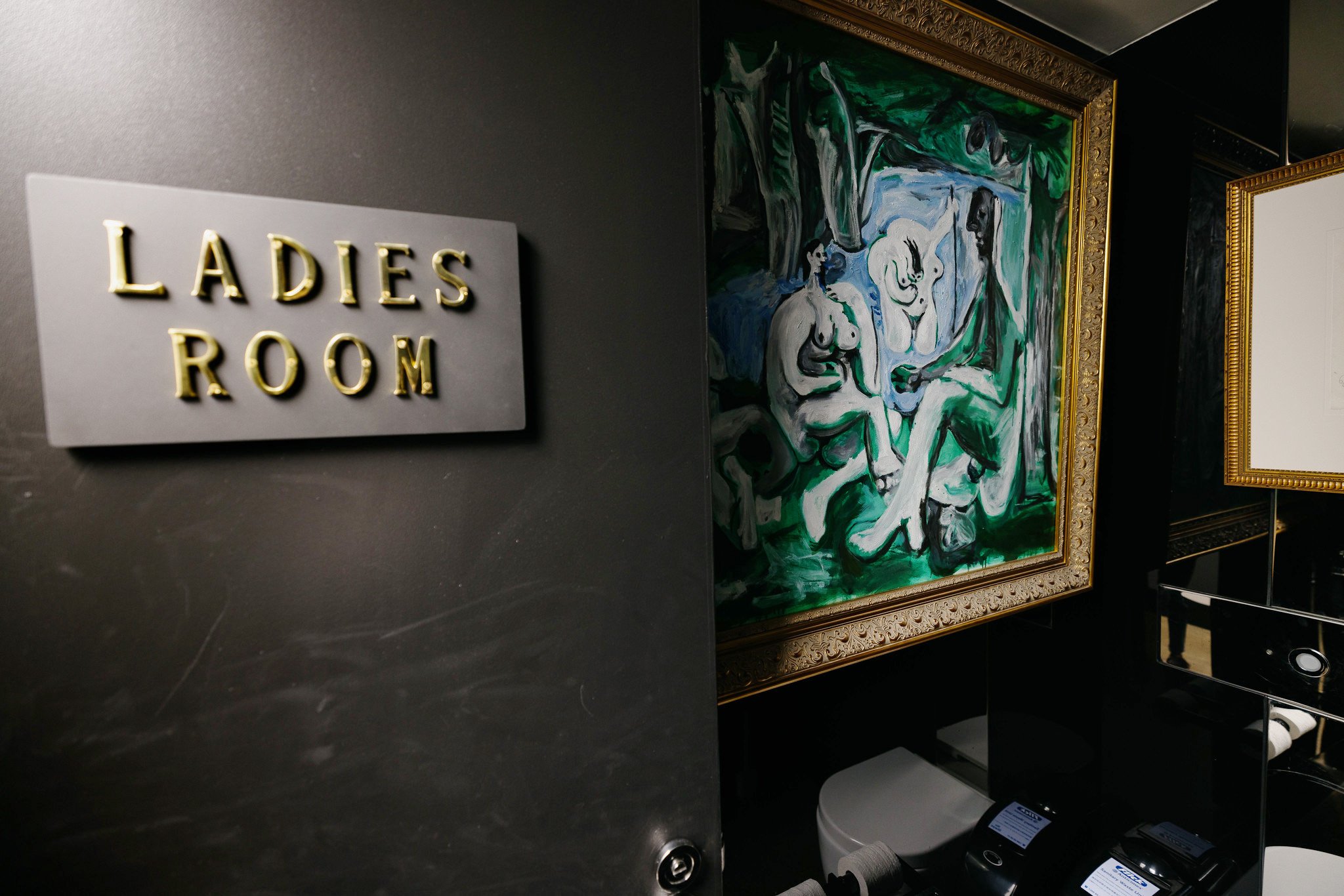 A Picasso hung inside a toilet, with its door reading "Ladies Room"