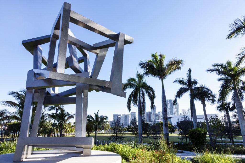 An angular sculpture against a backdrop of palm trees