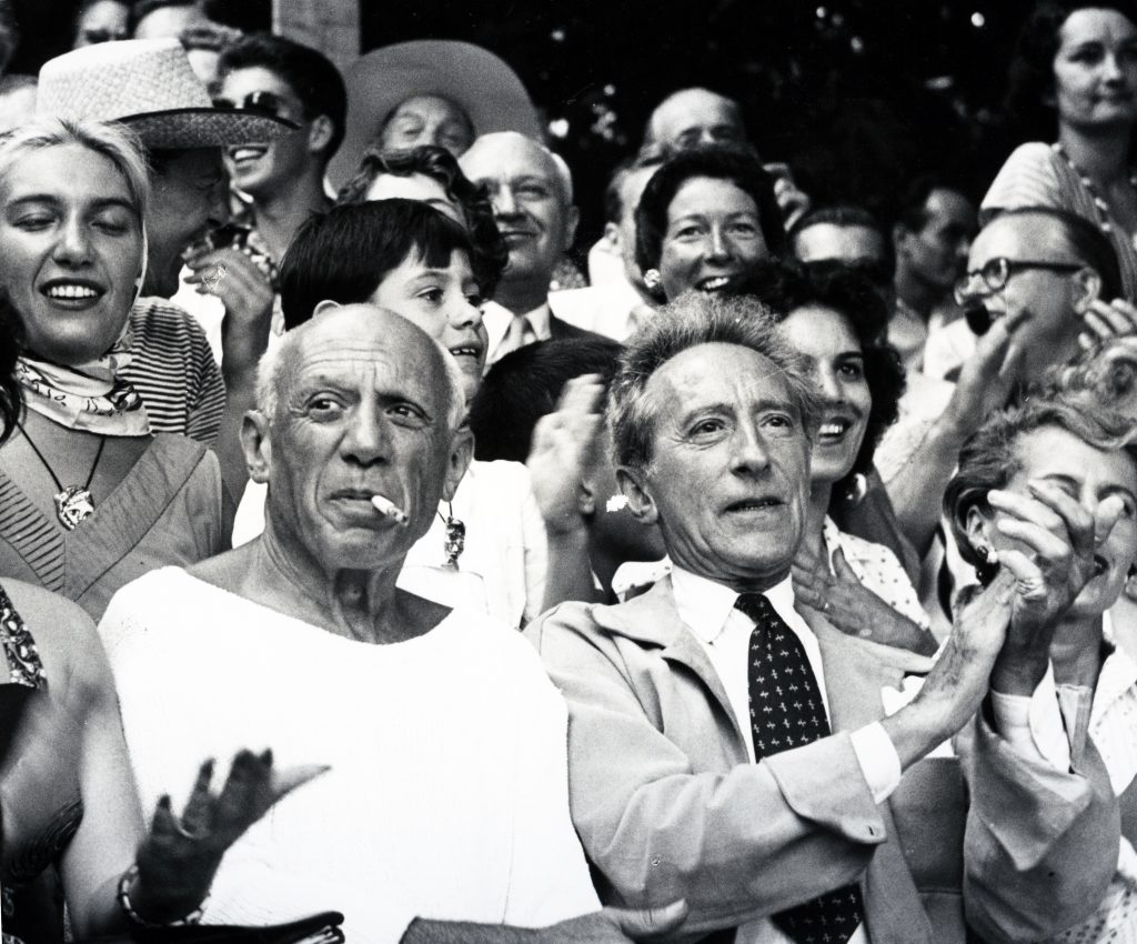 The painter Pablo Picasso is a focal point in a black and white crowd image watching a bullfight which is out of frame.