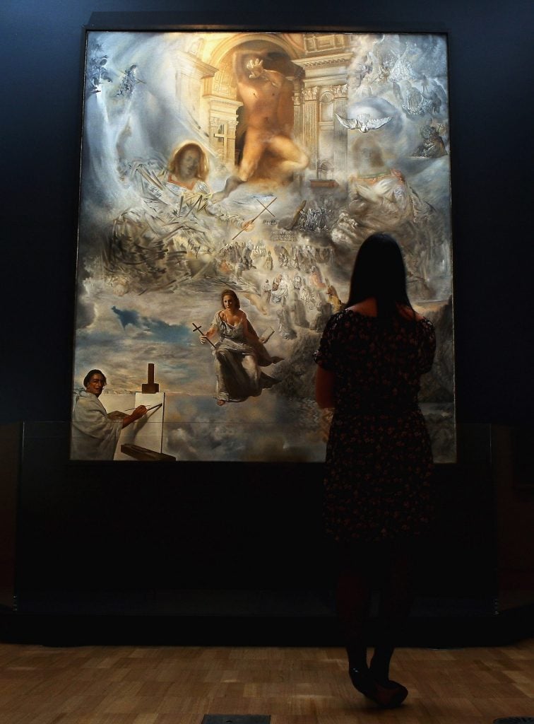 A woman stands in front of a large and complex religious painting in a darkened gallery