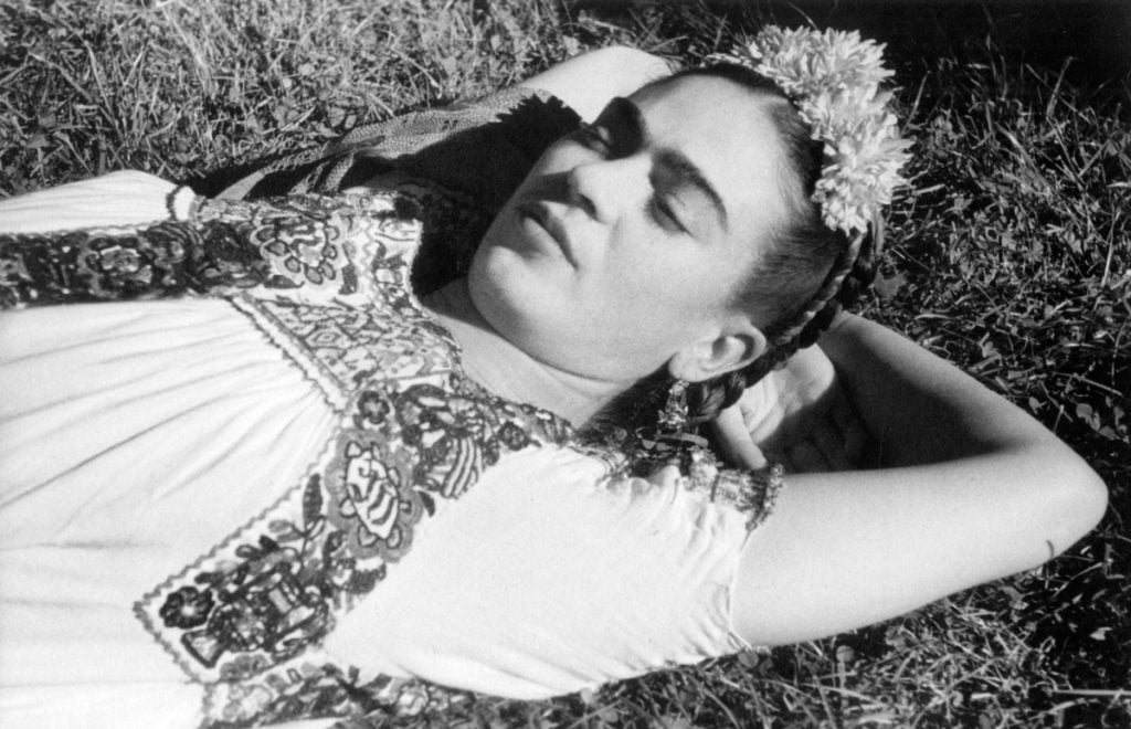 a black-and-white photograph of a woman lying on the grass, arms tucked behind her head, with flowers in her hair.