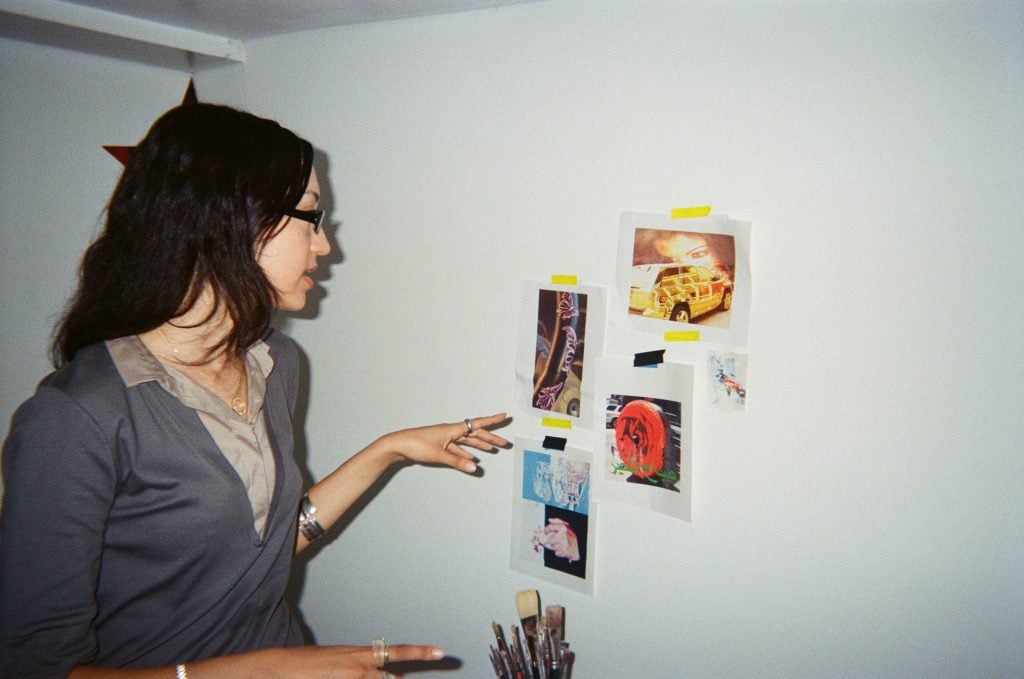 A woman points at images printed off on computer paper taped to a white wall