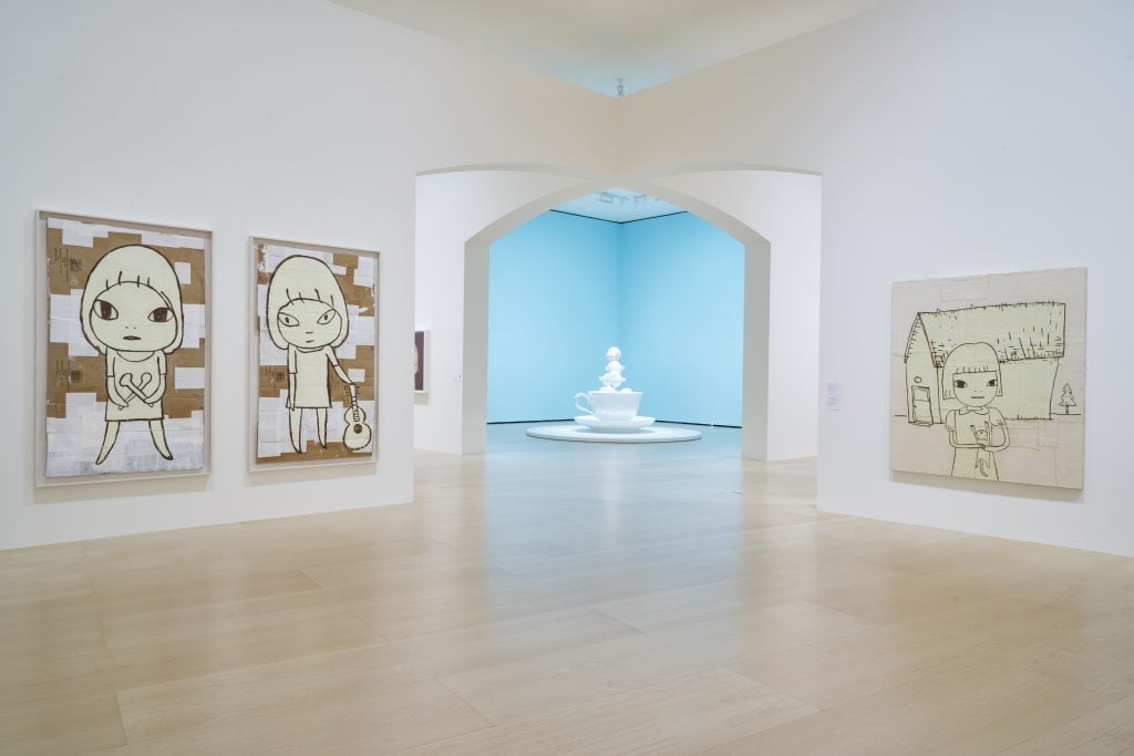 an art gallery features drawings on opposite walls. in the background, a light blue room with a large sculpture can be seen