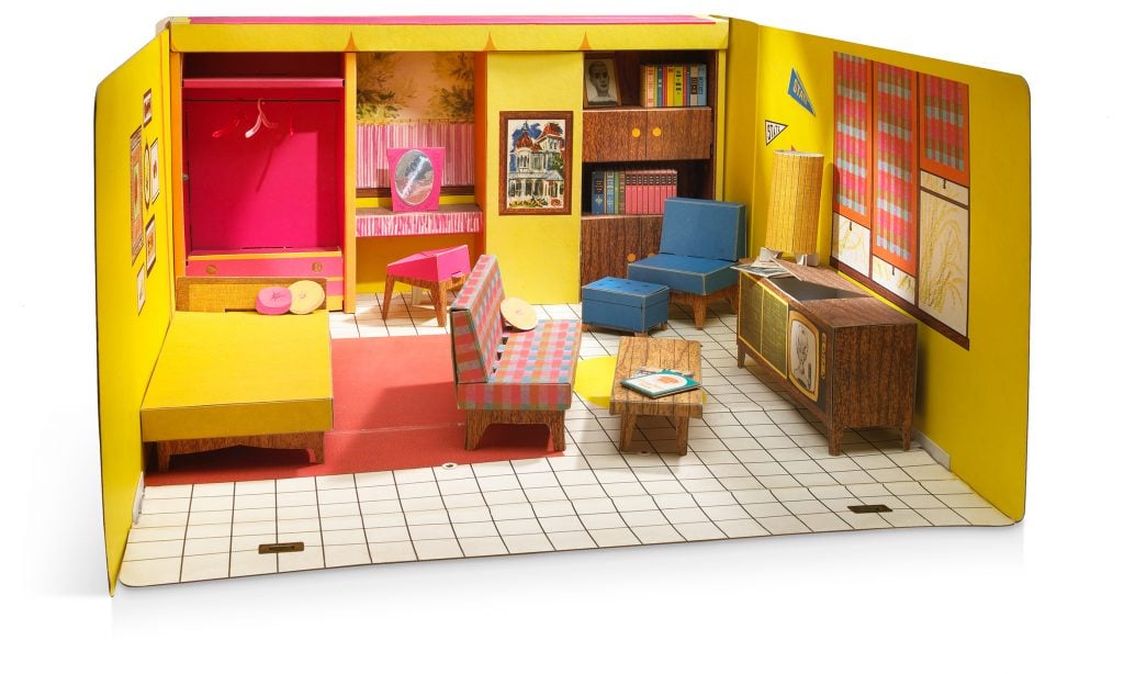 A cardboard dolls house room featuring yellow walls, a bed and a pink sofa