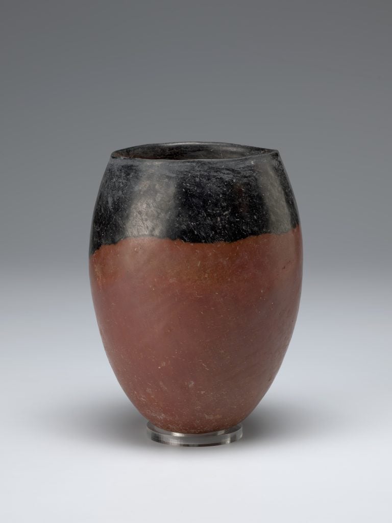 An ancient Egyptian jar characterized by its black-topped finish, smoothly transitioning to a reddish-brown body. The vessel has a rounded shape with a simple, unadorned design, indicative of its utilitarian purpose.