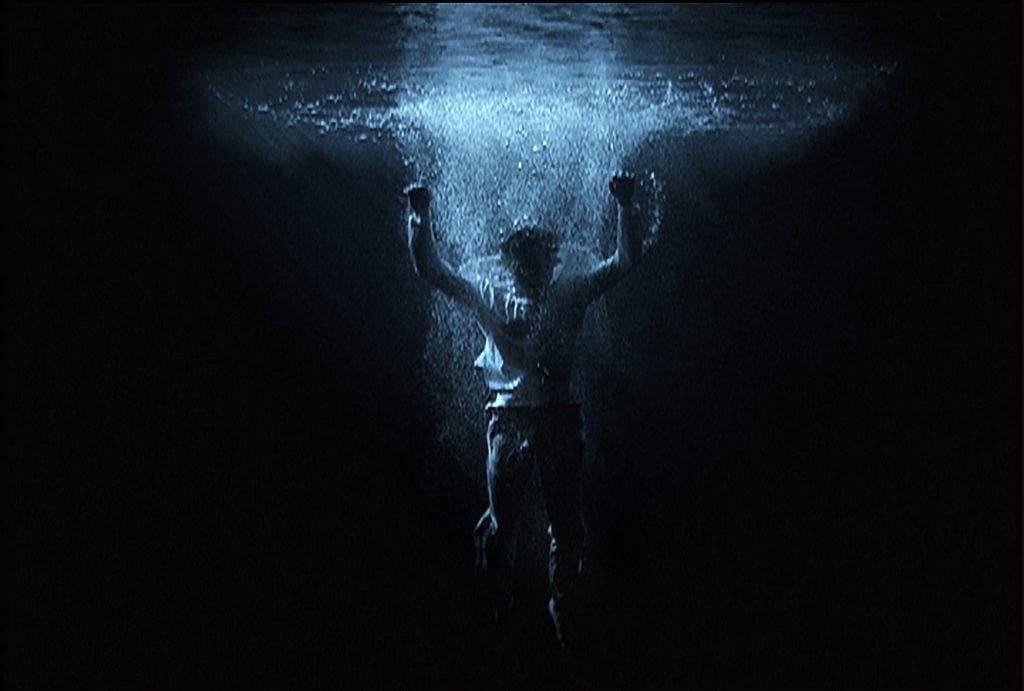 a male figure with arms raised is inside some water, its dark