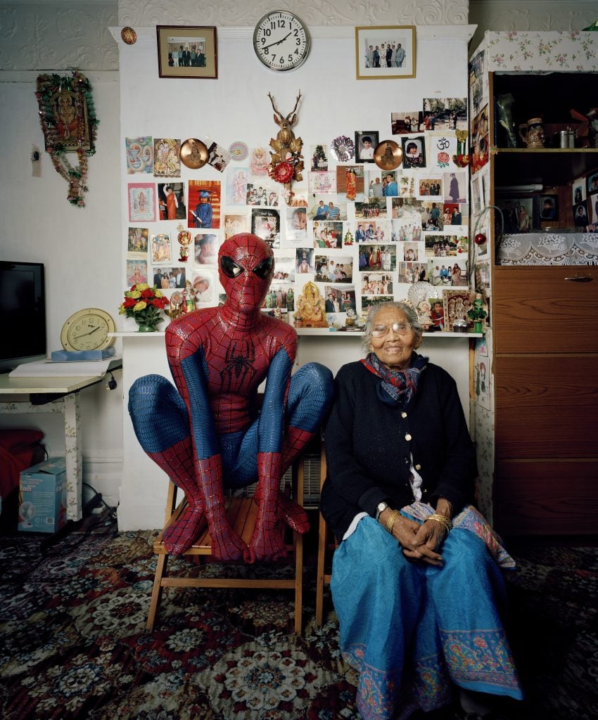 A man dressed as Spider-Man crouching next to an elderly woman.