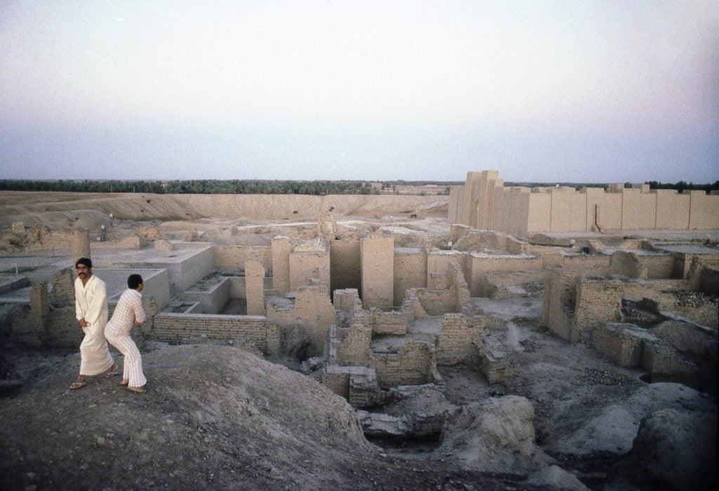 a view over the ancient city of Babylon with two men in the foreground and ruins in the background