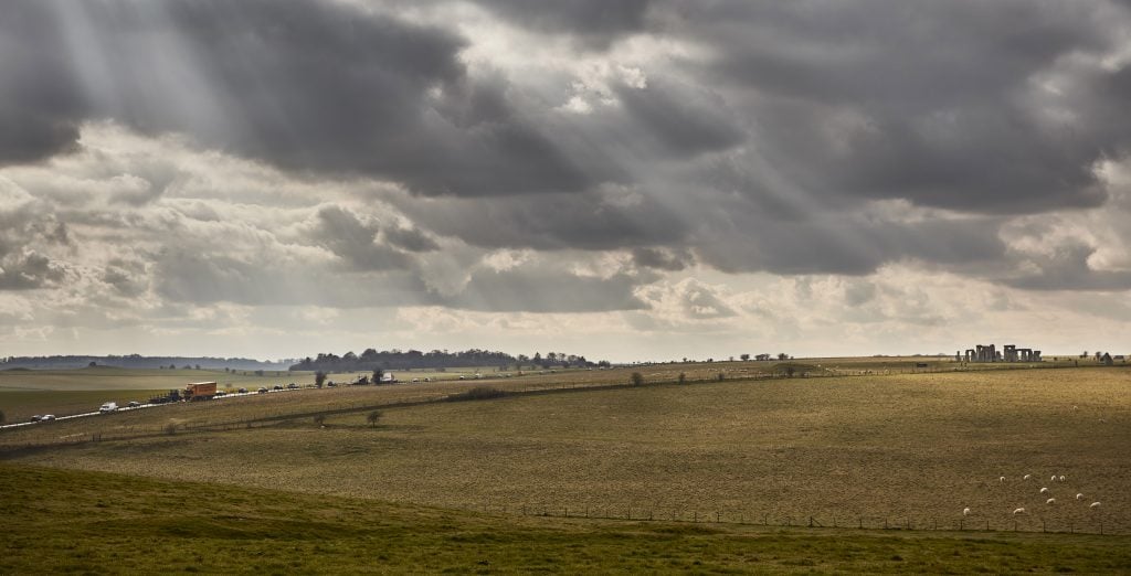 a photo of the british landscape with stonehenge in the distance and sheep in the foreground