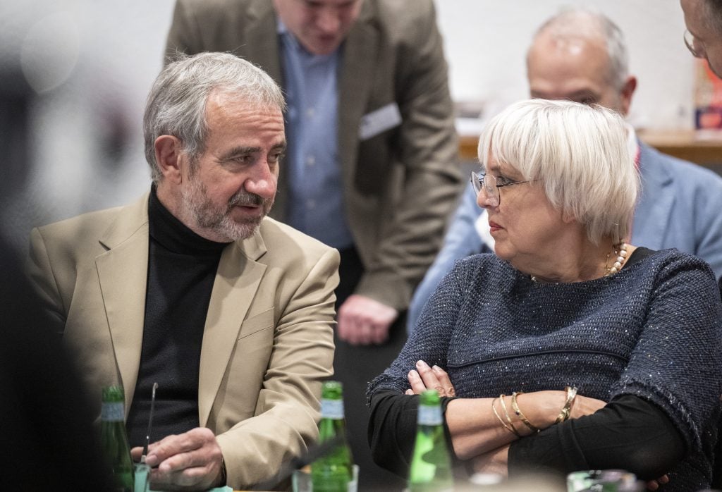 two people, a man and a woman, sitting next to each other looking at each other as though mid conversation