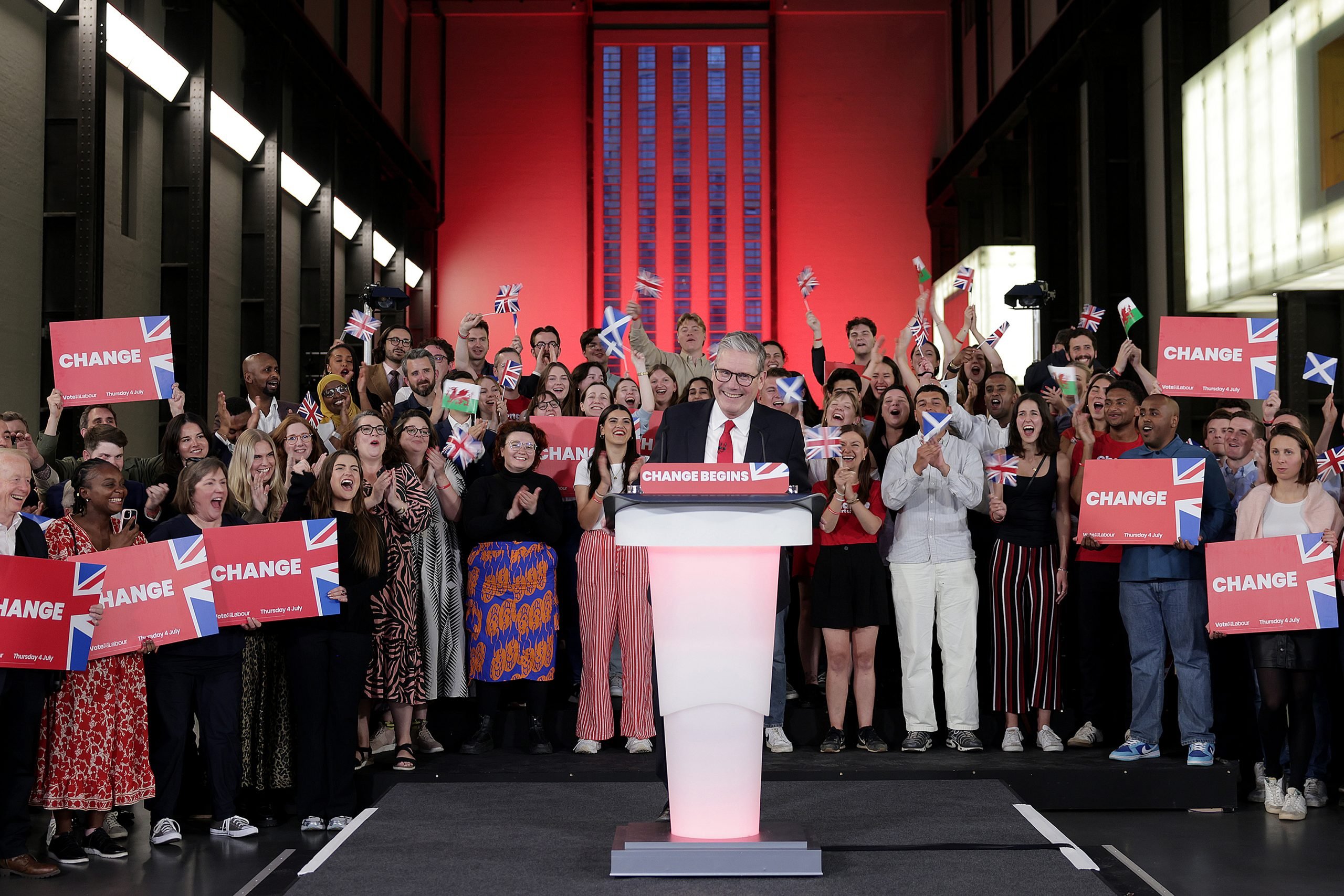 a man stands at a podium in a suit. a crowd of people surrounding him clap and hold signs that say CHANGE