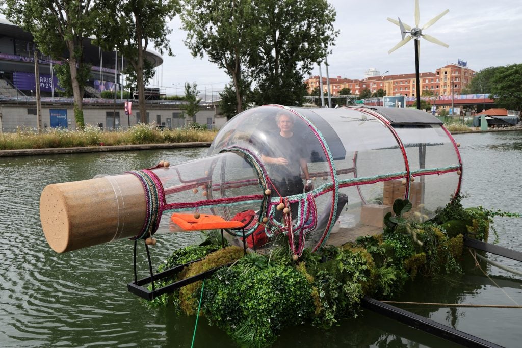 a giant bottle floats on a river with a man inside