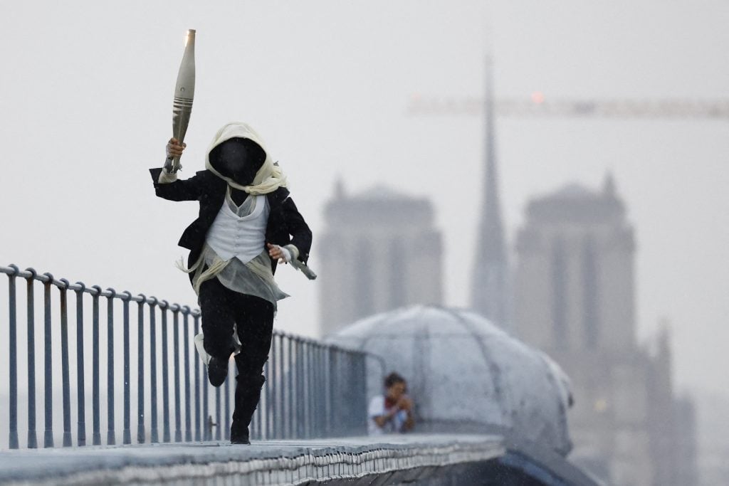 A masked torchbearer runs atop the Musee d'Orsay during the Opening Ceremony of the Olympic Games Paris 2024.