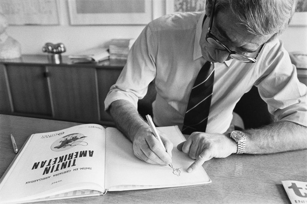 A black and white photograph of a man autographing a book about the character Tintin